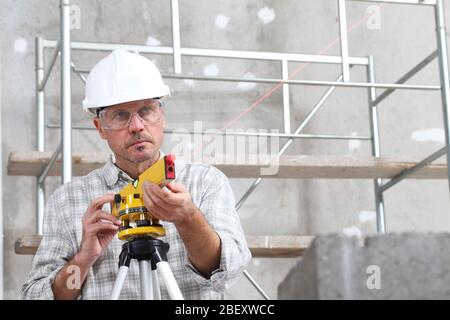 construction man worker measure with level laser wear hard hat and protective glasses  at interior building site Stock Photo