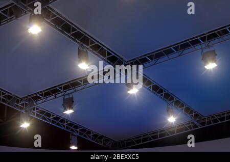 A row of four light projectors on a scene ceiling with cables and metal supports Stock Photo