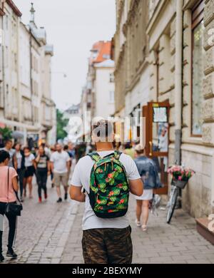 A man with a backpack on a city tour in the summer. A young man walks the city on a sunny day. Sports guy in shorts and with a colored backpack Stock Photo