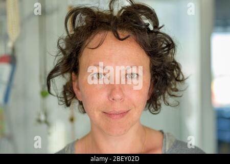 Hispanic woman with tousled curly hair standing indoors in the bathroom smiling at the camera in a close up portrait Stock Photo