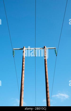 A wooden high voltage electricity pole with glass insulators seen against a blue sky, in the UK countryside Stock Photo