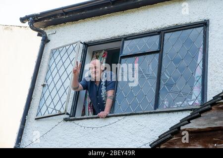 Slough, Berkshire, UK. 16th April, 2020. A man makes a peace sign from his window. He is one of the vulnerable people who has to stay at home for three months following medical advice on shielding for those with certain medical conditions during the Coronavirus Pandemic in England. Credit: Maureen McLean/Alamy Live News