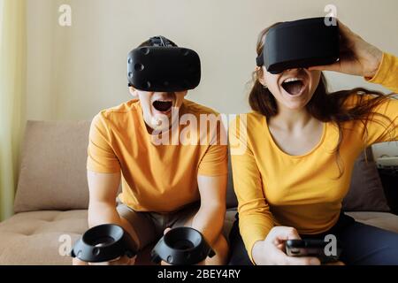 What to do at home. A guy and a girl play virtual games. People are wearing virtual reality helmets for game.  Stock Photo