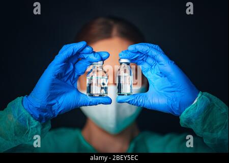 Female doctor or scientist hold two medical glasses in front of eyes. Medicine bottle for injection medical glass vials and syringe for vaccination. C Stock Photo