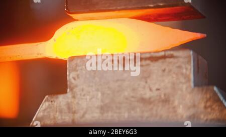 Blacksmith making a knife out of hot metal using a pressure machine. Mid shot Stock Photo