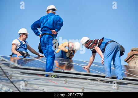Male team engineers installing solar photovoltaic panel system. Electricians mounting blue solar module on roof of modern house. Alternative energy ecological concept. Stock Photo