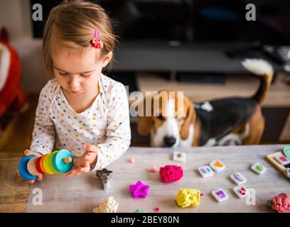 Happy little child, adorable creative 2 year old girl playing with dough, colorful modeling compound, sitting bright sunny room at home. Stock Photo