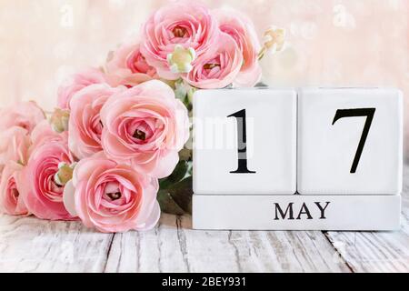 Generic white wood calendar blocks with the date May 17th and pink ranunculus flowers over a wooden table. Selective focus with blurred background. Stock Photo