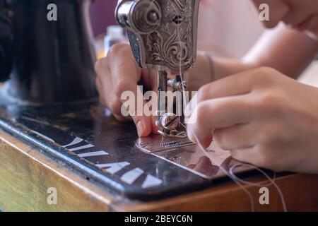 A seamstress inserts a thread into a needle eye on an old retro sewing machine. Focus on the eye of the needle. Horizontal. Stock Photo