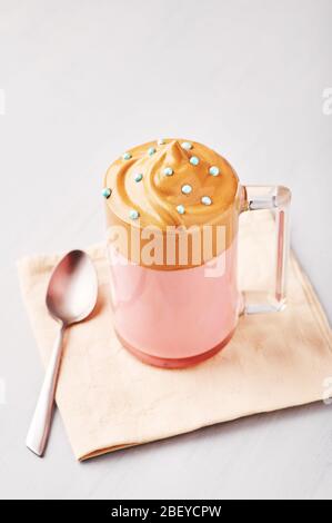 Pink milk Dalgona Coffee decorated with blue Easter sprinkles in a glass cup at bright grey background. Dalgona Frothy Coffee is a Korean trendy drink Stock Photo
