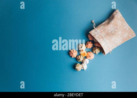 Colorful meringues and a small cloth bag decorated with white snowflakes on a blue background. Selective focus. Stock Photo