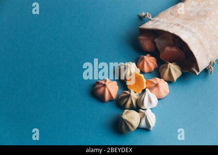 Colorful meringues and a small cloth bag decorated with white snowflakes on a blue background. Selective focus. Stock Photo