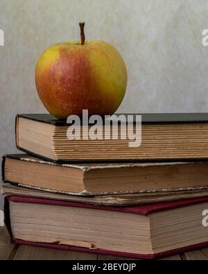 A wrinkled apple over classical books on wooden desk against brown background, viewed from the side, to illustrate the concept of outtraded or vintage Stock Photo