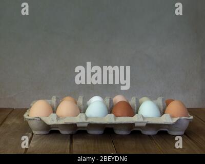 One dozen unwashed colorful chicken eggs in open cartonon on wooden surface viewed from the side and plenty of copy-space- free-range eggs of various Stock Photo