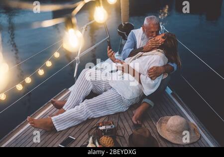 Senior couple kissing during sailboat vacation - Happy mature people having tender moments celebrating wedding anniversary on boat trip