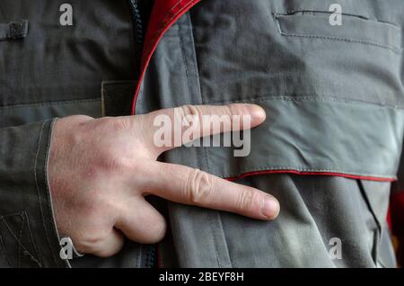 Man Shows Two Finger Gesture. A middle-aged man in work clothes shows the number two with his fingers. Eye level shooting. Selective focus. Close-up. Stock Photo