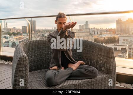 Young Man in Lotus Pose At Skyscraper Roof Relaxing From Stress At Quarantine and Isolation From Coronavirus Pandemia, Keeping Social Distance and Goo Stock Photo