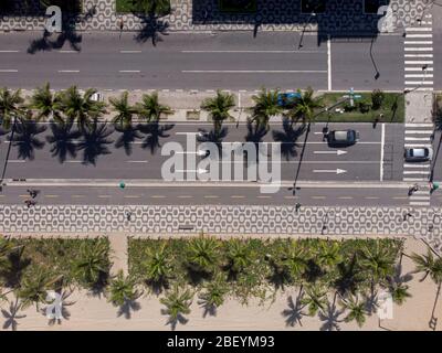 Top down aerial view of Ipanema boulevard with cars passing on the avenue flanked by palm trees and pedestrian crossing with people biking and walking Stock Photo