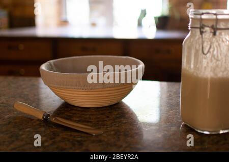 Sourdough starter and proving basket on top of a kitchen work surface with a palette knife Stock Photo