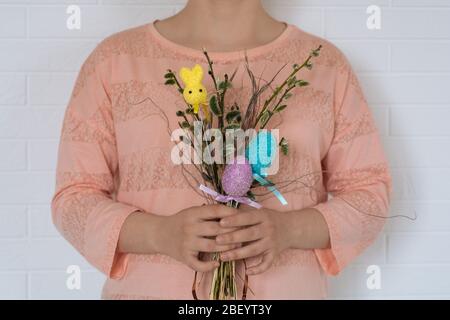 a young girl in a pink t-shirt holds an Easter bouquet of branches with chicken eggs and a rabbit on the white wall background. Horizontal view Stock Photo