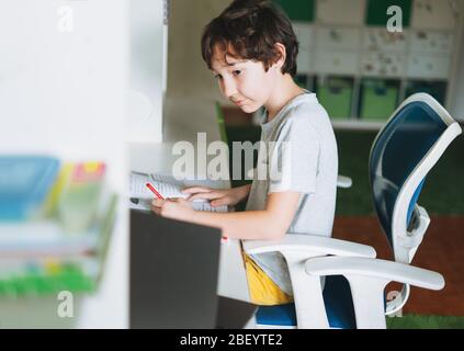 Tween boy do homework learn foreign language writing in pupil book with opened laptop at the room home dictance education Stock Photo