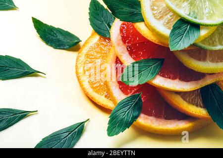 Citrus lemon, lime, orange and grapefruit slices and mint leaves in pile on yellow background. Minimal design background. Stock Photo