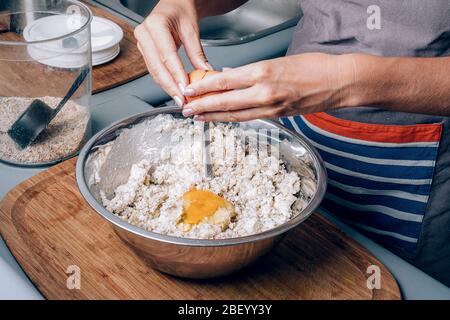 Woman's hands crushing an egg and putting it into flour while making homemade pastry. Stock Photo