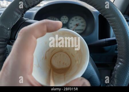 view of the bottom of an empty Cup of cocoa drunk in the driver hand on the background of the steering wheel and dashboard of the car Stock Photo