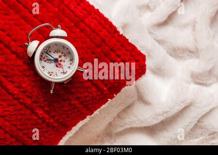Close up of a red pillow and alarm clock on white blanket background Stock Photo