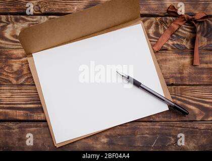 One Craft envelop, white paper into it  and black pencil  on old brown wooden  table Stock Photo