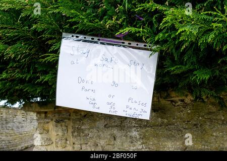 Chippenham, Wiltshire UK, 16th April, 2020. With the nation due to once again clap to show their support for the NHS tonight, a childs handwritten sign telling people to stay in and stay safe is pictured on a hedge in Chippenham, Wiltshire. Credit: Lynchpics/Alamy Live News Stock Photo