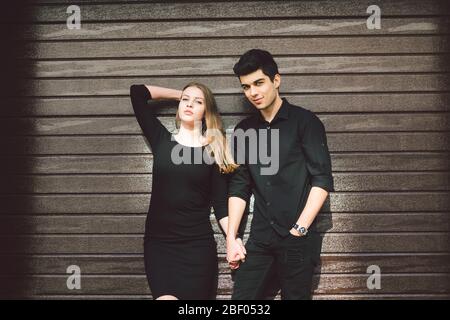 Multiracial stylish couple in black clothes posing on a background of a wooden wall. Turkish guy and caucasian girl date and love. Muslim man and Stock Photo