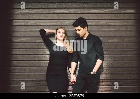 Multiracial stylish couple in black clothes posing on a background of a wooden wall. Turkish guy and caucasian woman date and love. Lifestyle Stylish Stock Photo