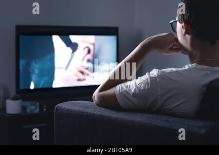 Horror movie stream on tv. Man watching scary film or series on online streaming or VOD service in dark home living room at night. Stock Photo