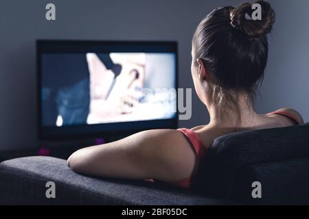 Young woman watching horror movie on online stream service. Girl streaming scary film or series at night. Fear and terror during thriller on tv. Stock Photo