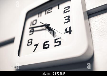 Modern clock on a wall. Almost 5 o'clock in the afternoon or morning. Over time at work. Dramatic angle. Stock Photo