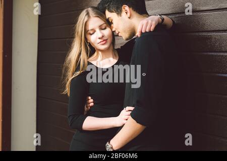 Multiracial stylish couple in black clothes posing on a background of a wooden wall. Turkish guy and caucasian woman date and love. Lifestyle Stylish Stock Photo