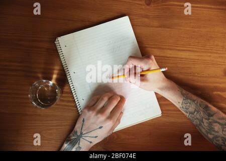 Close up of male hands writing on an empty paper on the table at home. Making notes, workhome, report for his work. Education, freelance, art and business concept. Leaves signature, doing paperwork. Stock Photo