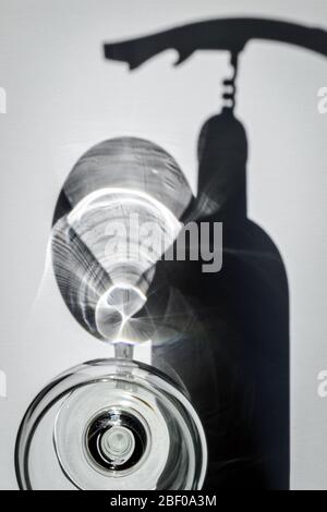 Shadows of a bottle of wine and glass, and shadow of hand and corkscrew on a white textured surface. Ready to drink wine. Stock Photo