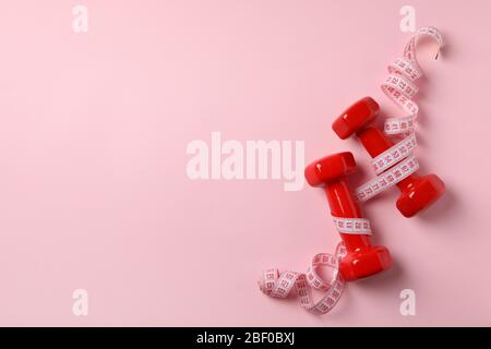 Dumbbells and measuring tape on pink background, space for text Stock Photo