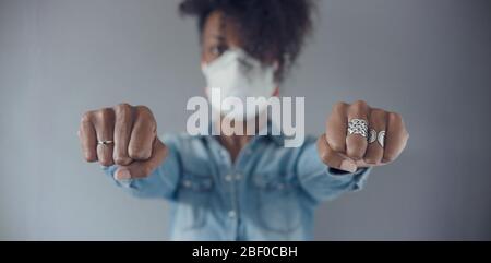 Black woman wearing a FFP3 mask. Concept of fight against coronavirus, Covid-19. Selective focus on her left fist.