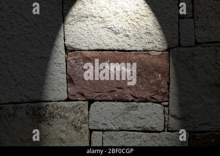 Wall built with rectangular stone. There is a red stone in the middle, Stock Photo