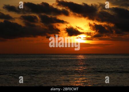 Sunset over the sea, orange sun is reflected in dramatic waves. Colorful sky with dark clouds, romantic background for travel and vacations Stock Photo