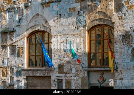San Gimignano, Tuscany: Two windows and flags on the facade of the medieval Palazzo Comunale (or Palazzo del Popolo) in the Piazza del Duomo. Stock Photo