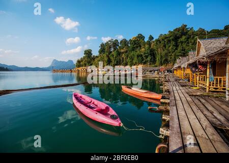 Wooden traditional thai longtail boat on Cheow Lan lake arriving to floating bungalow huts in Khao Sok National Park, Thailand