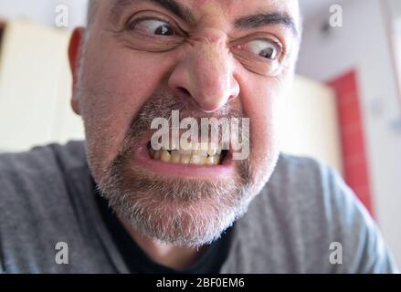 Portrait of an extremely angry middle-aged Caucasian man: bloodshot eyes are staring down at the side. The gritted teeth and the curled nose in the ex Stock Photo