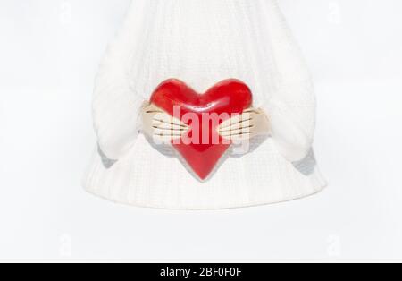 A white ceramic-figure of an angel in a long robe holds a big red heart with both hands. Charity and sharing concept. Stock Photo