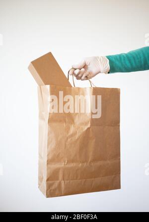 grocery store shopping delivery man giving paper bag wearing blue glove as protection for COVID-19 Coronavirus precautions. Stock Photo