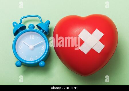 Toy heart with adhesive plaster and alarm clock on a green background, top view. The concept is time to treat the heart Stock Photo