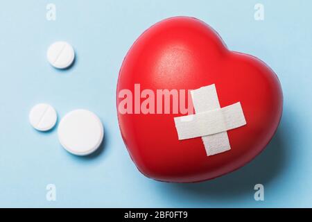 Pills and adhesive plaster on a toy heart, top view. Concept for taking medicine for heart disease Stock Photo